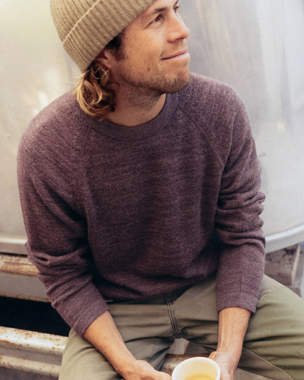 Seated three-quarter view of The Original Crew alpaca crewneck sweater in raisin showing soft knit texture, raglan sleeves and relaxed fit on a model