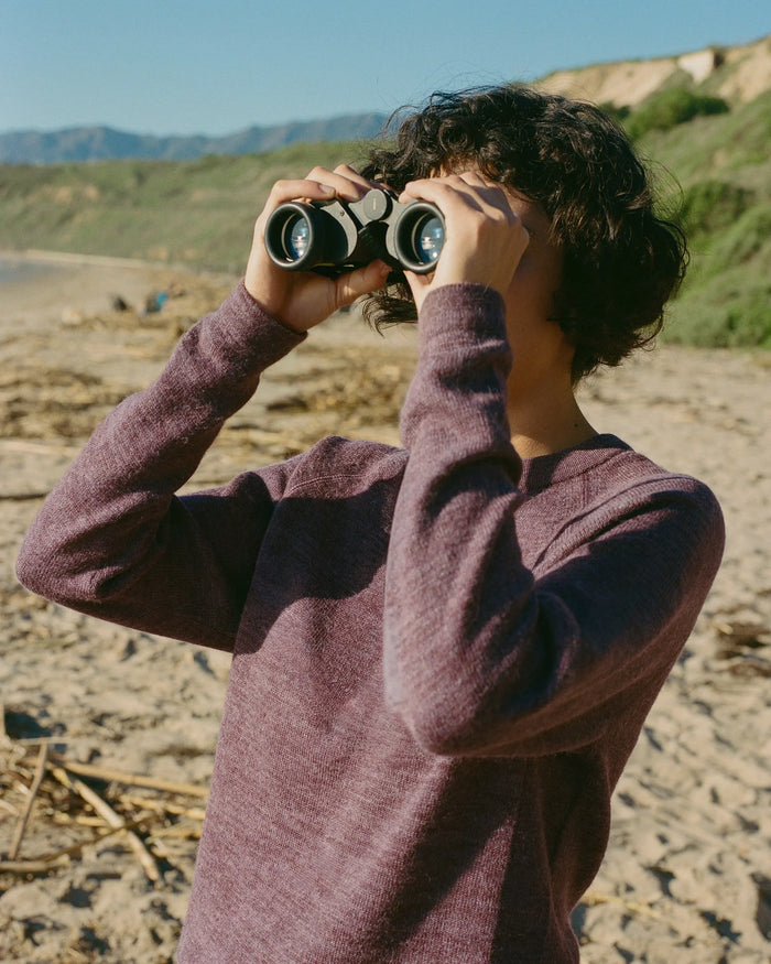 Three-quarter front view of The Original Crew alpaca crewneck sweater in Raisin showing soft knit on a model at the beach