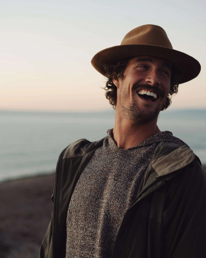 The Vida hoodie in brown marled knit on a model, showing relaxed fit and ergonomic hood at the beach