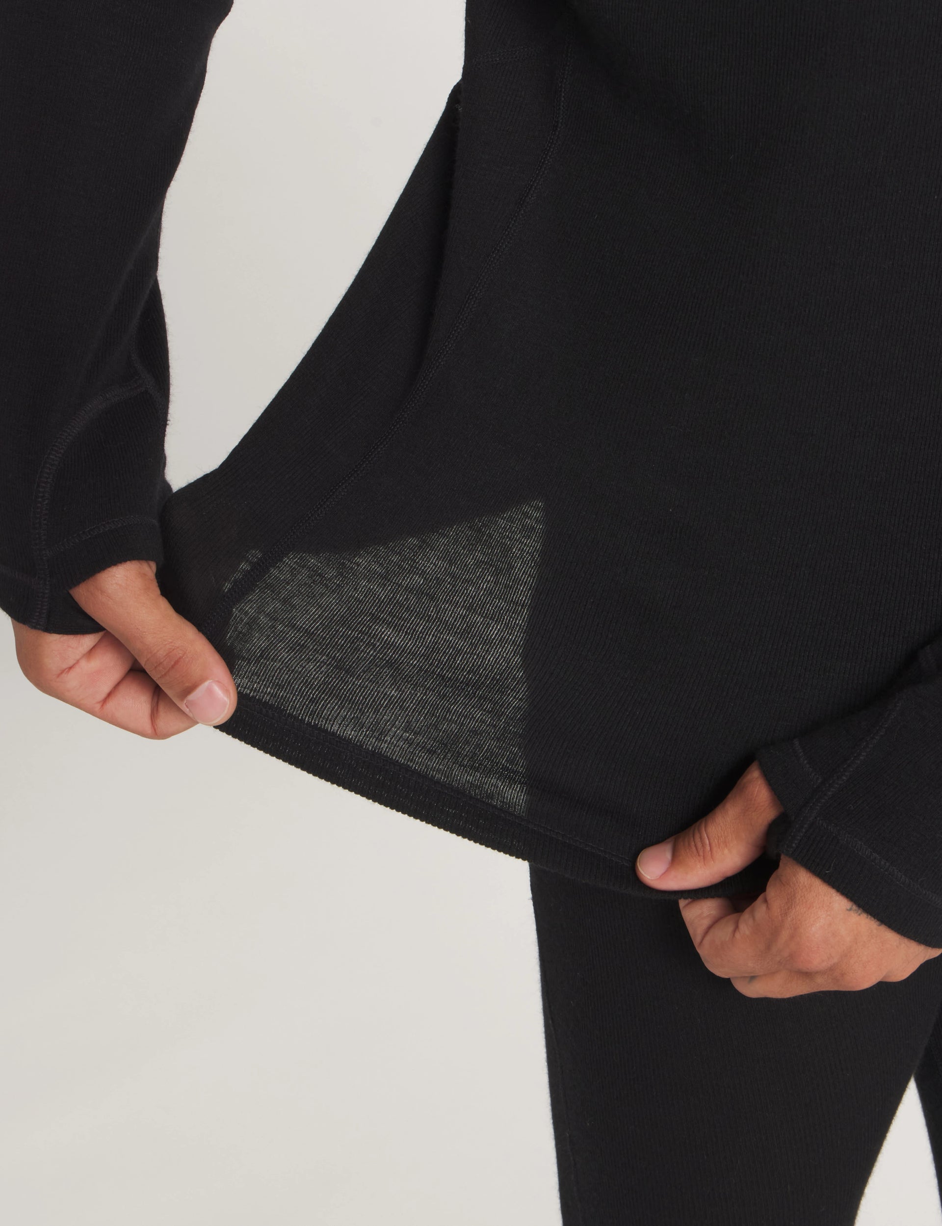Close-up of black women’s thermal top hem stretched to show rib knit and flatlock seam on neutral background