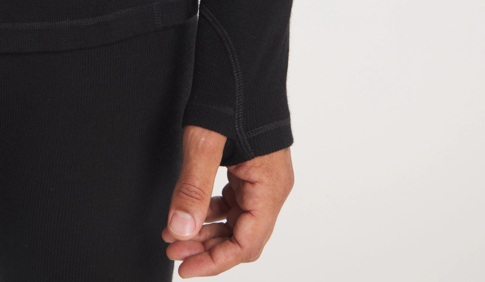 Close-up of a black women’s thermal top sleeve showcasing a thumb hole and flatlock stitching against a light background