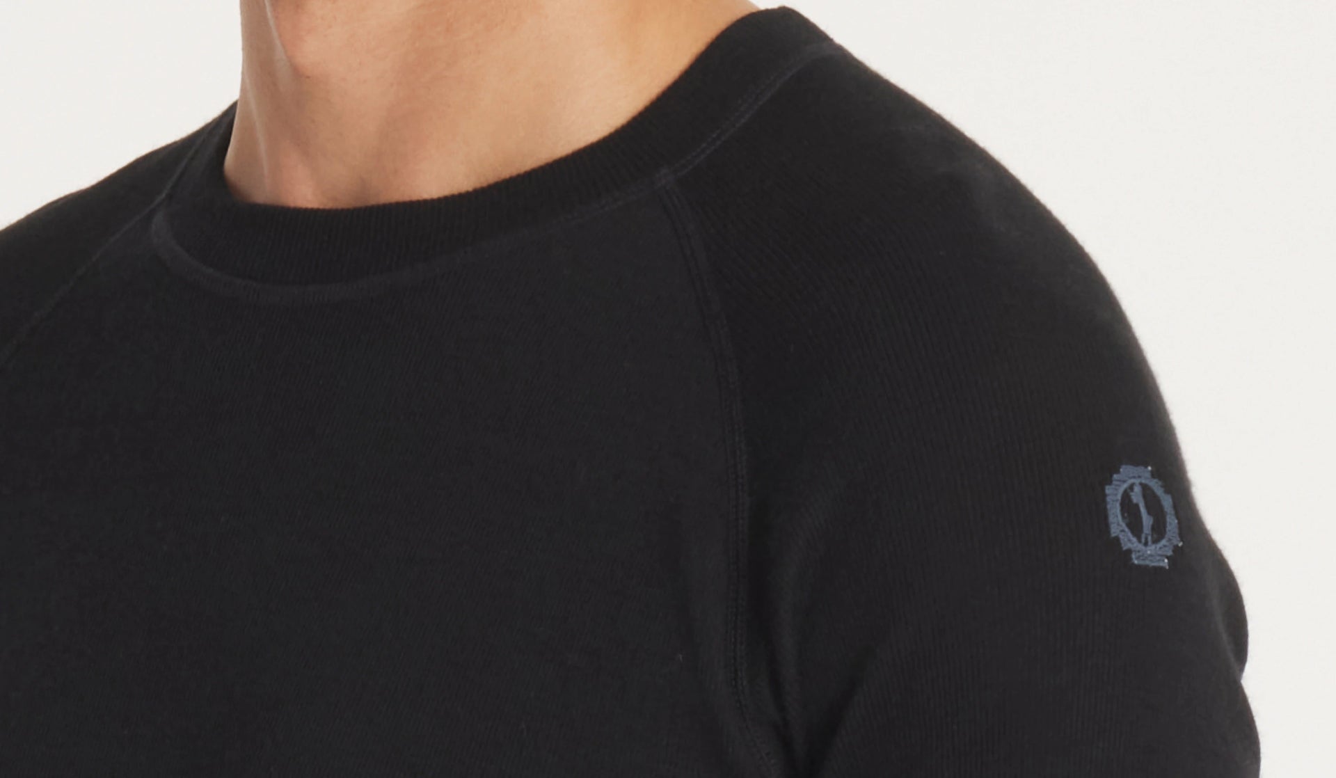 Close-up front view of women’s black thermal top showing ribbed crew neck, raglan shoulder seam, knit texture, and small sleeve logo