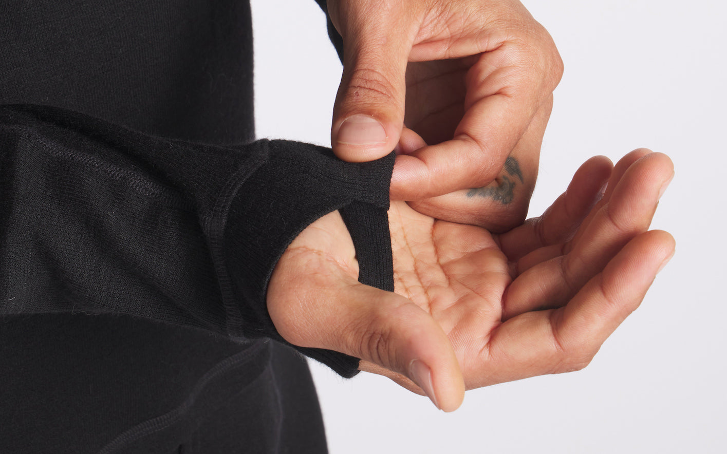 Close up of black men’s thermal baselayer sleeve showing thumbhole cuff and flatlock seam on white background