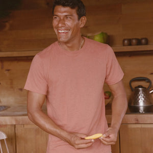 Man in a pink shirt holding a banana in a kitchen.