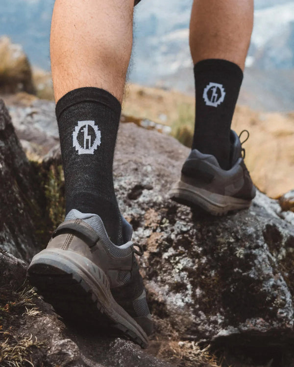 Back view of black Trail 3/4 crew socks on model showing mid-calf coverage and white logo with rocky hiking trail background