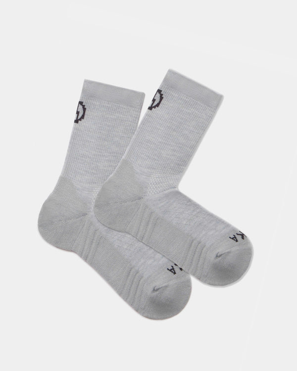 Flat lay of Trail 3/4 crew socks in light gray showcasing cushioned sole and black PAKA logo on cuff and toe on white background