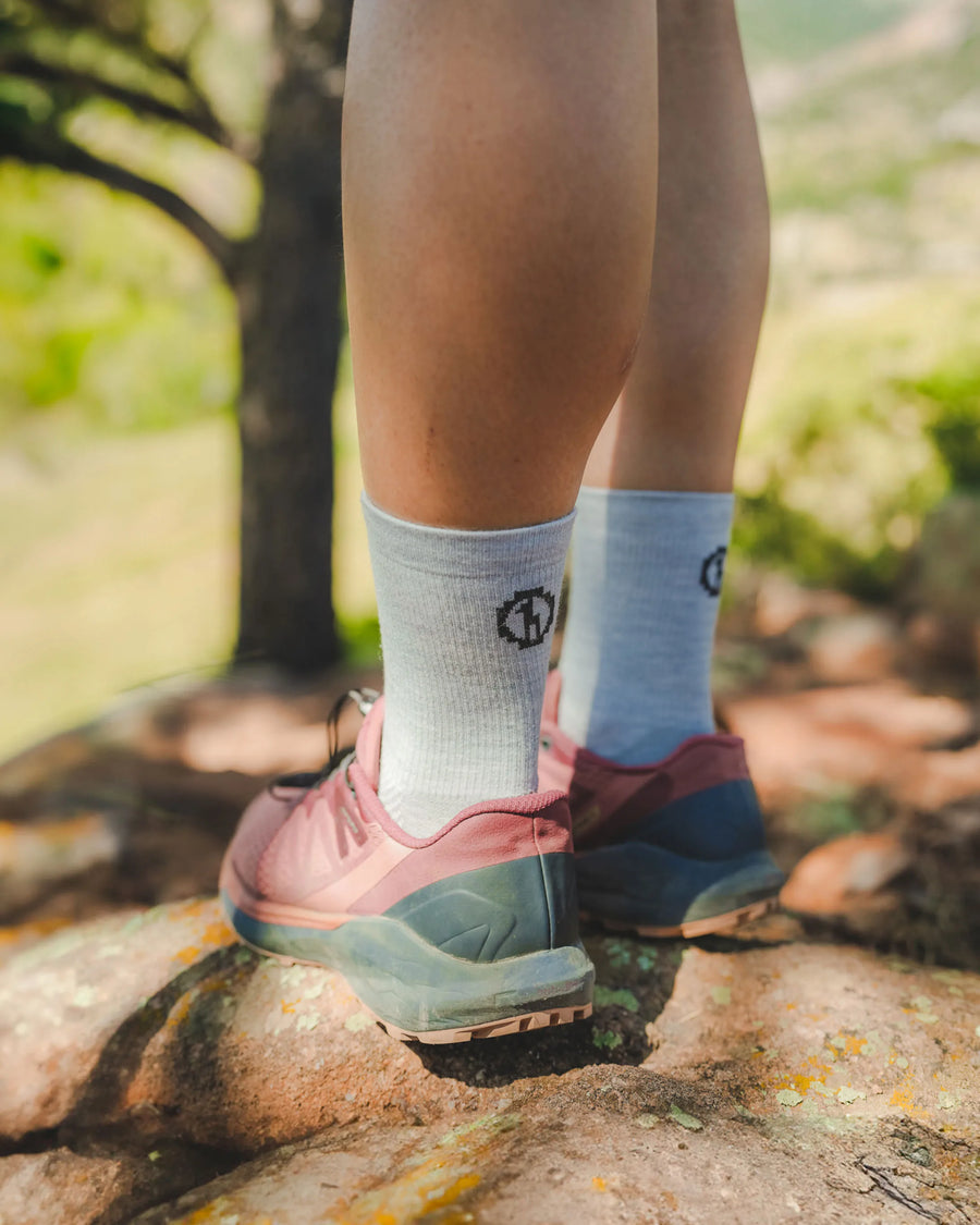 Rear view of light gray 3/4 crew hiking socks on a model showing mid-calf height and cushioned knit, worn on a rocky trail