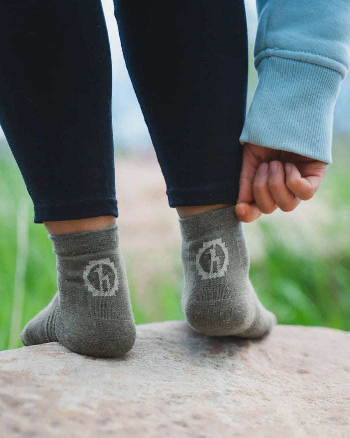 Rear view of Trail 1/4 Crew lightweight hiking socks in charcoal blue on a model showing ankle height and heel logo on a rock