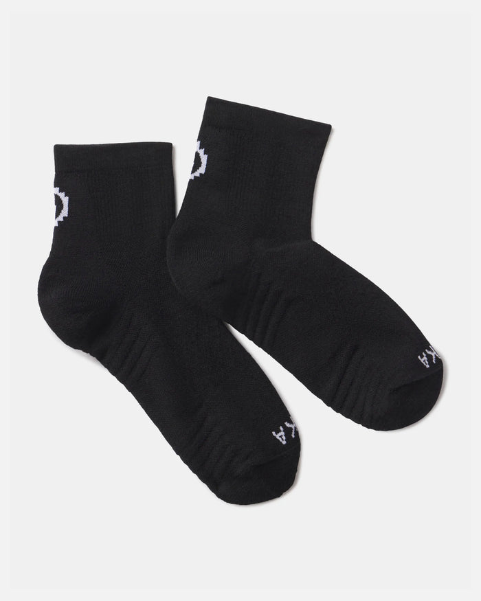 Flat lay of Trail 1/4 crew socks in black showcasing white PAKA logo and ribbed cushioned footbed on a light gray background
