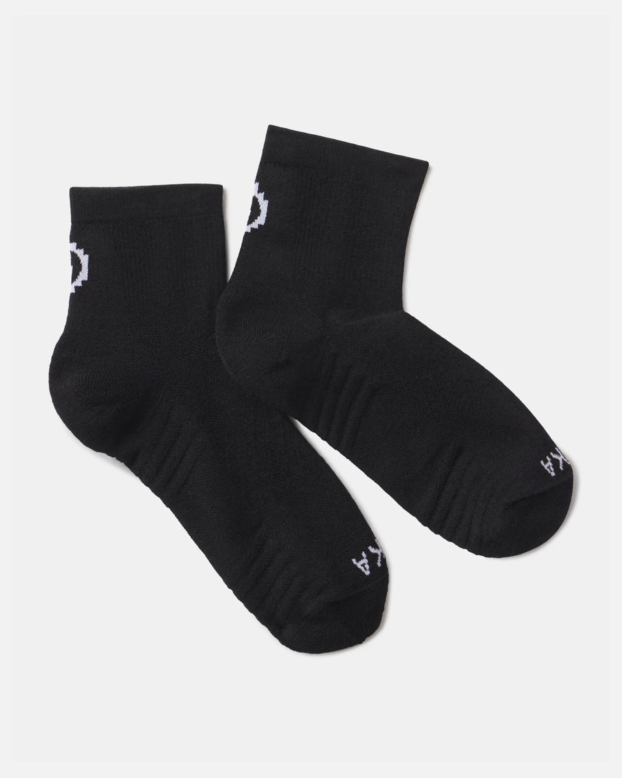 Flat lay of Trail 1/4 crew socks in black showcasing white PAKA logo and ribbed cushioned footbed on a light gray background