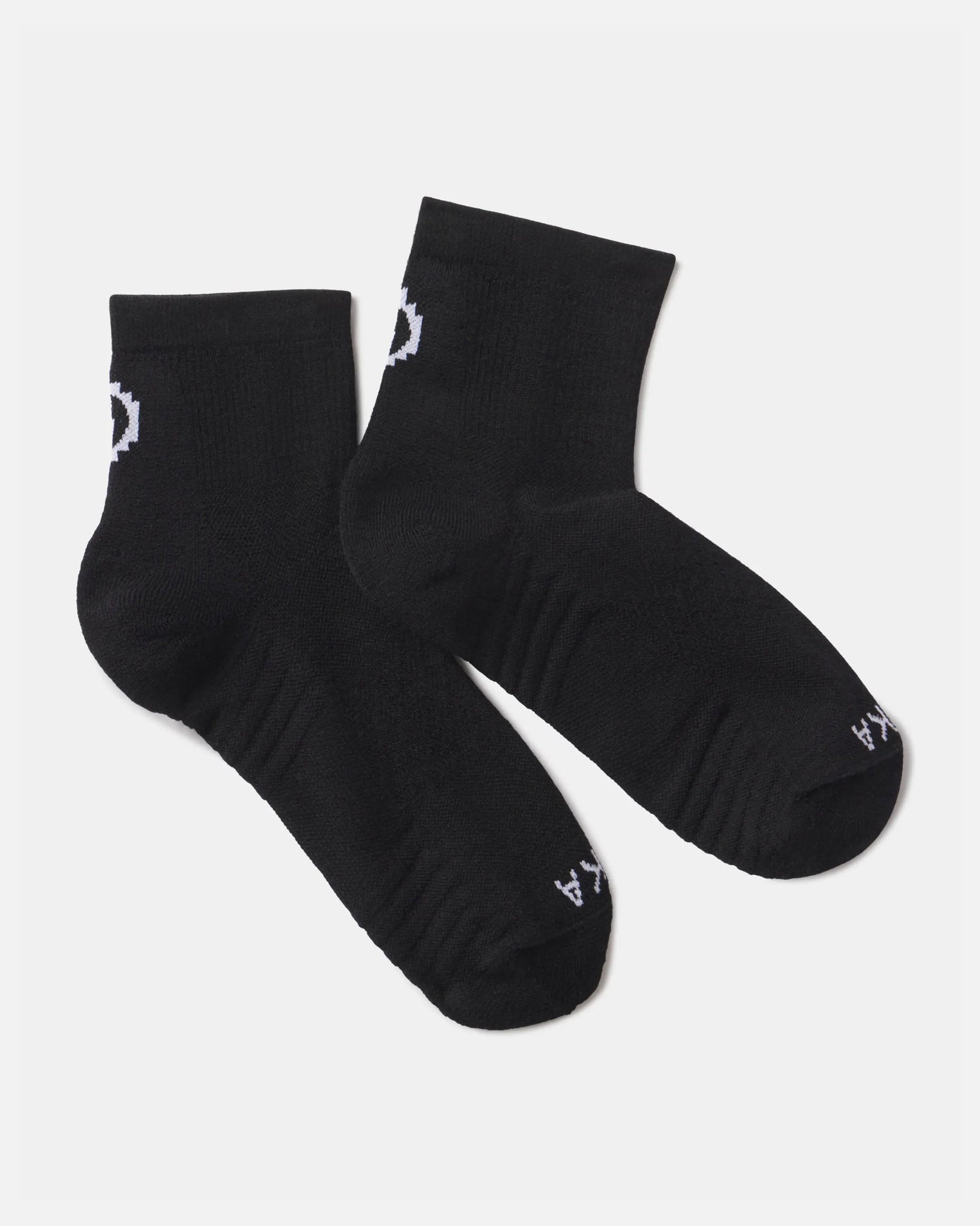 Flat lay of Trail 1/4 crew socks in black showcasing white PAKA logo and ribbed cushioned footbed on a light gray background
