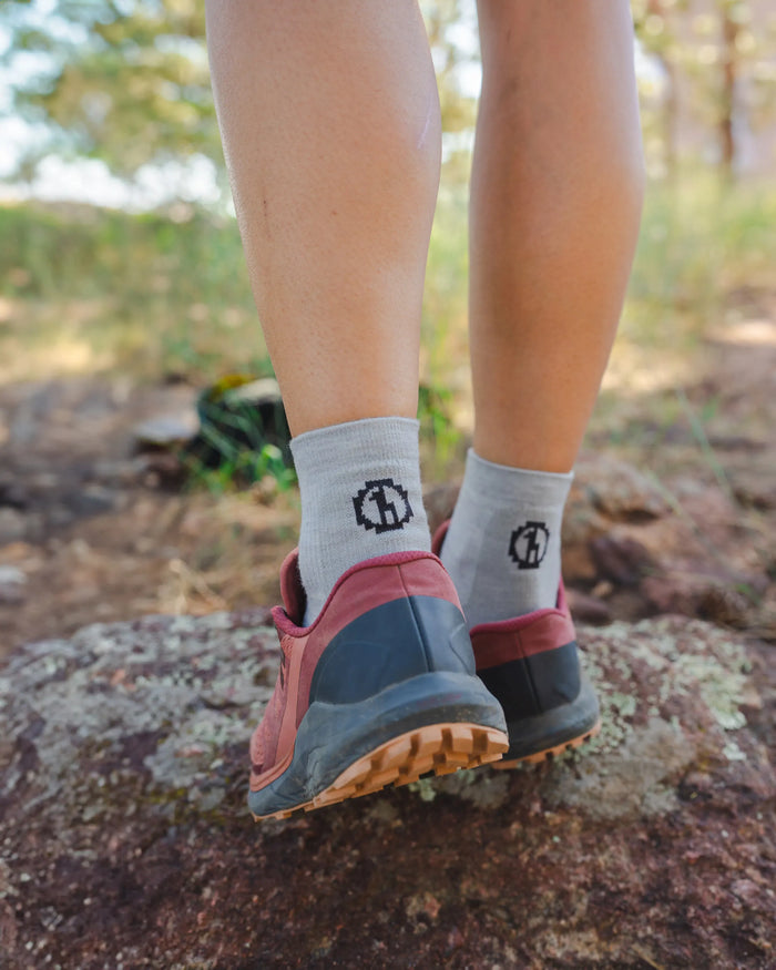 Rear view of Trail 1/4 crew hiking socks in charcoal blue on a model showing ankle height with outdoor rock background