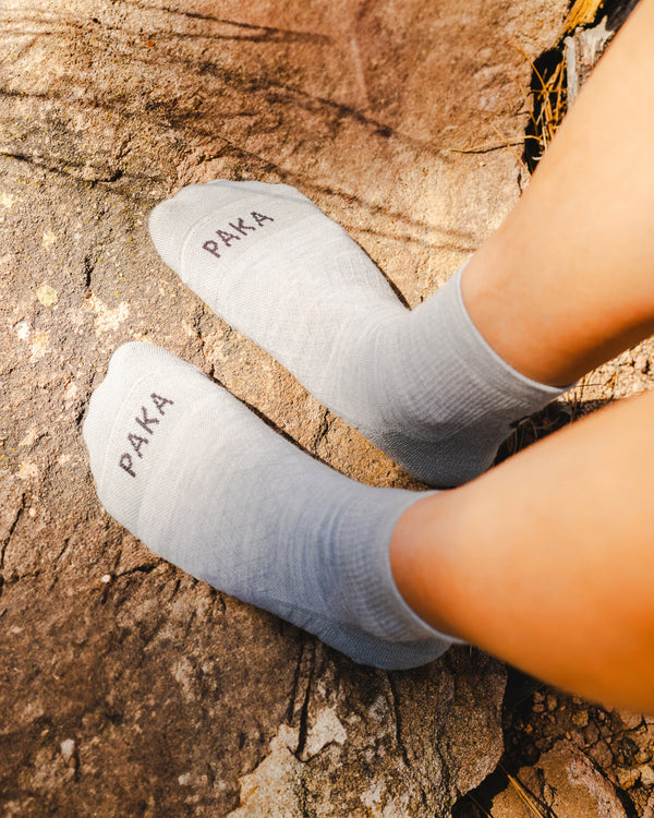 Top-down view of Trail 1/4 Crew socks in charcoal blue on feet showing 1/4 crew fit and PAKA logo on toes on rocky background