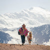 A man in a colorful poncho walking with an Alpaca in front of Ausangate