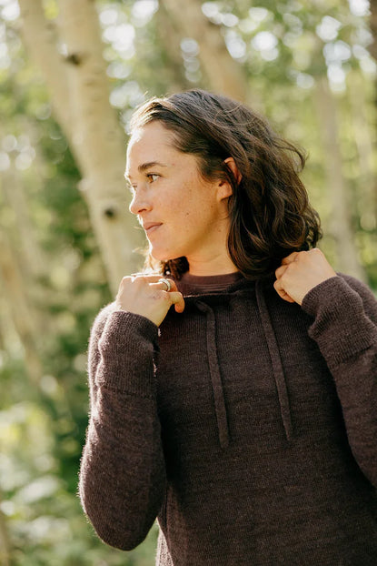 Three-quarter view of women’s hoodie on model showcasing feminine fit and soft alpaca knit with sunlit forest background