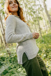 Side view of women’s light gray hoodie showcasing feminine fit, curved hem and side slit with sunlit forest background
