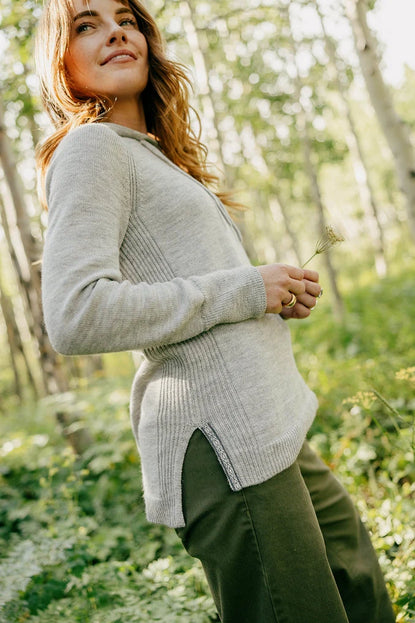 Side view of women’s light gray hoodie showcasing feminine fit, curved hem and side slit with sunlit forest background