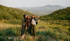 Three women wearing earth-toned women’s hoodies (relaxed fit) walking together in a grassy hillside landscape