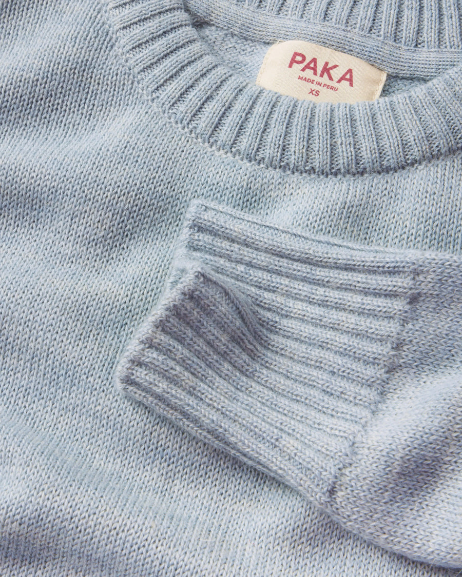 Close-up of a light blue sweater with a PAKA label on a matching background