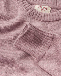 Close-up of Women’s Original Crew alpaca crewneck showing ribbed cuff, knit texture, and PAKA label on woodrose background