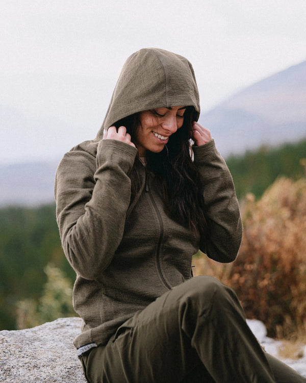 Three-quarter view of Women’s Breathe Full Zip alpaca hoodie in Andean Moss on seated model, zip front and hood