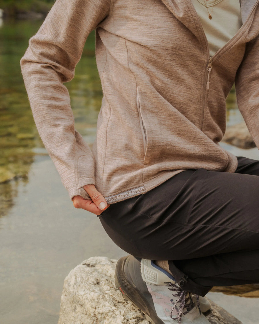 Side view of Women’s Breathe Full Zip Hoodie showcasing textured alpaca fabric, full front zipper, and side pocket with a lakeside rock background