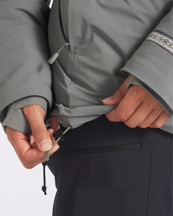 Close-up of women’s Apu Parka showing hem drawcord adjustment and thumbhole cuff on grey jacket against white background