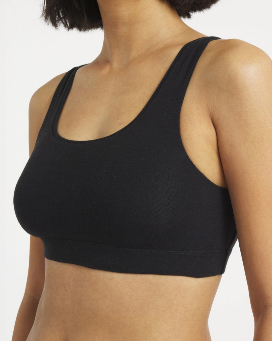 Three-quarter view of black scoop bralette on model, fitted, with scoop neckline, wide straps and elastic underband on white