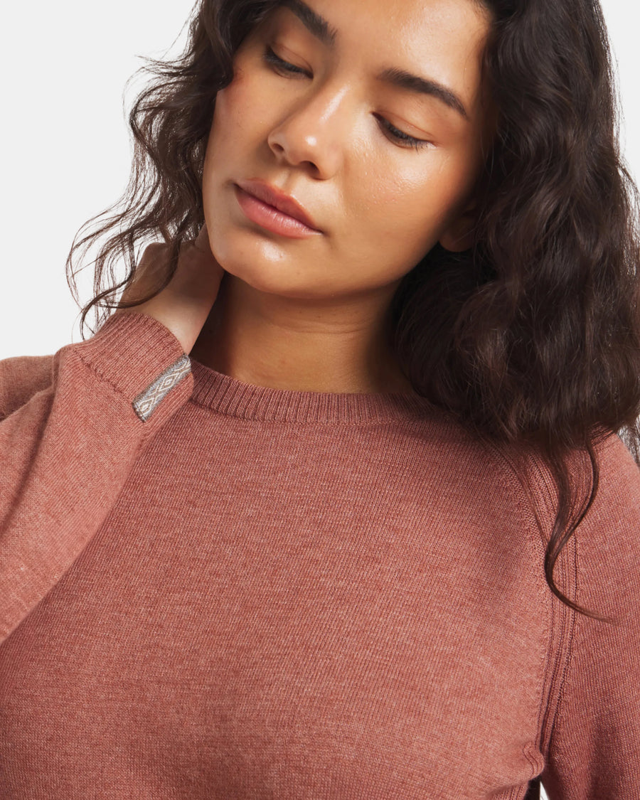 Close-up of a person wearing a cinnamon sweater with a brand logo on a white background