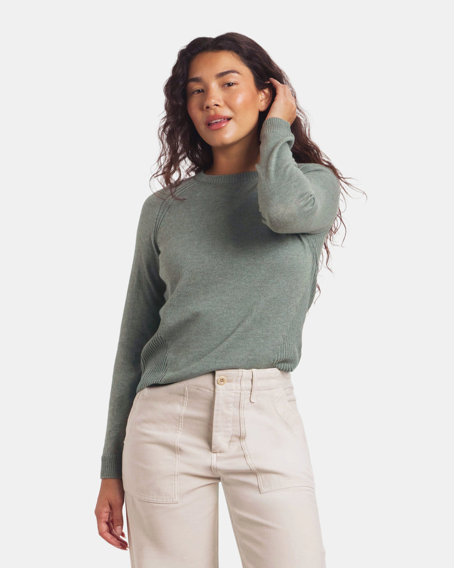 Woman wearing a green sweater and beige pants on a white background