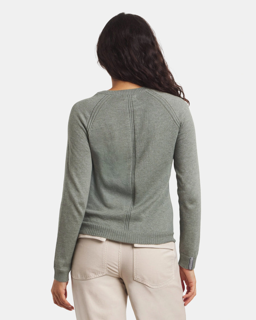Person wearing a green sweater and beige pants on a white background
