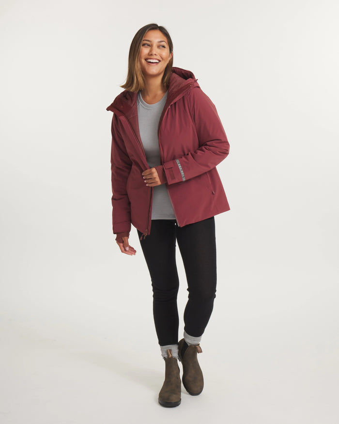 Three-quarter view of Women’s Apu Parka, Burgundy, hooded insulated ski jacket with hip-length fit on model, white background