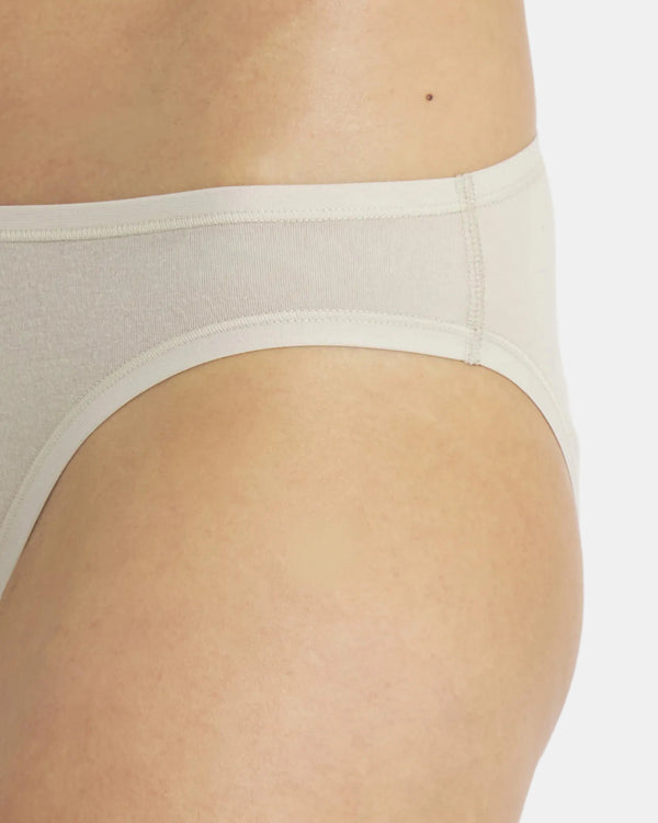 Side view of Women’s Essential Bikini Brief in bone showcasing mid-rise coverage and flat seam detailing on a model against a light gray background