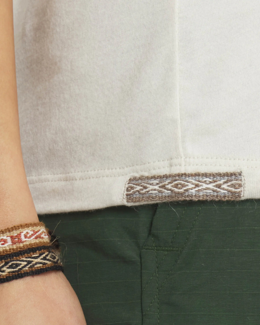 Close-up of Women’s Essential Tee hem in bone showing woven Inca ID tag and ribbed stitch with green pants background
