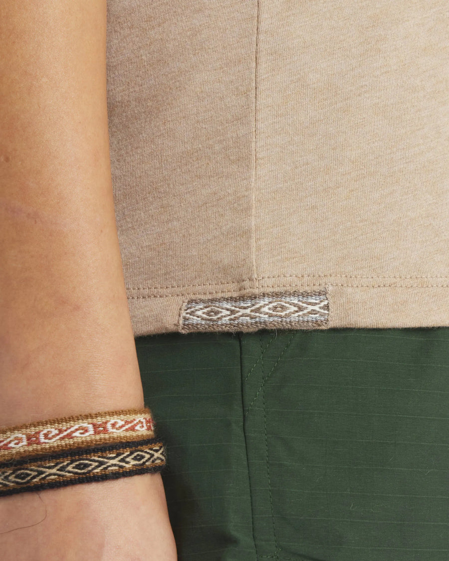 Close-up of Women’s Essential Tee hem showing woven Inca ID tag and side seam with model’s green pants and patterned bracelets