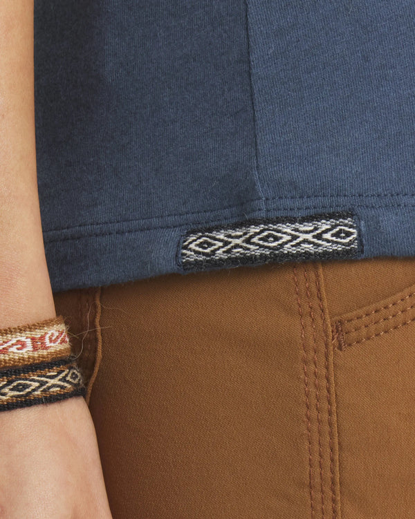 Close-up of Women’s Essential Tee (navy) showing woven Inca ID hem tag and ribbed hem over brown pants