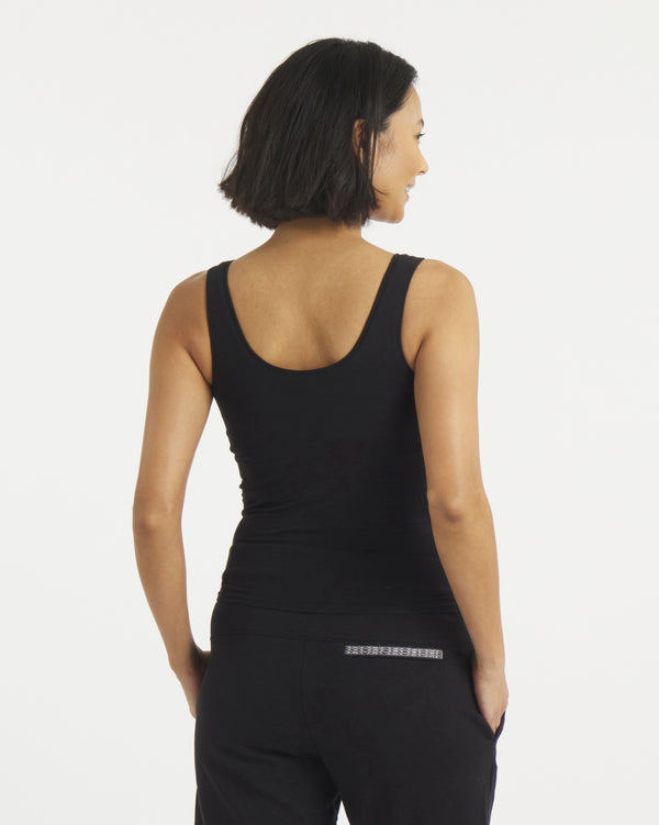 Rear view of Women’s Essential Tank in black showing cropped fit, wide straps, and built-in shelf bra on gray background