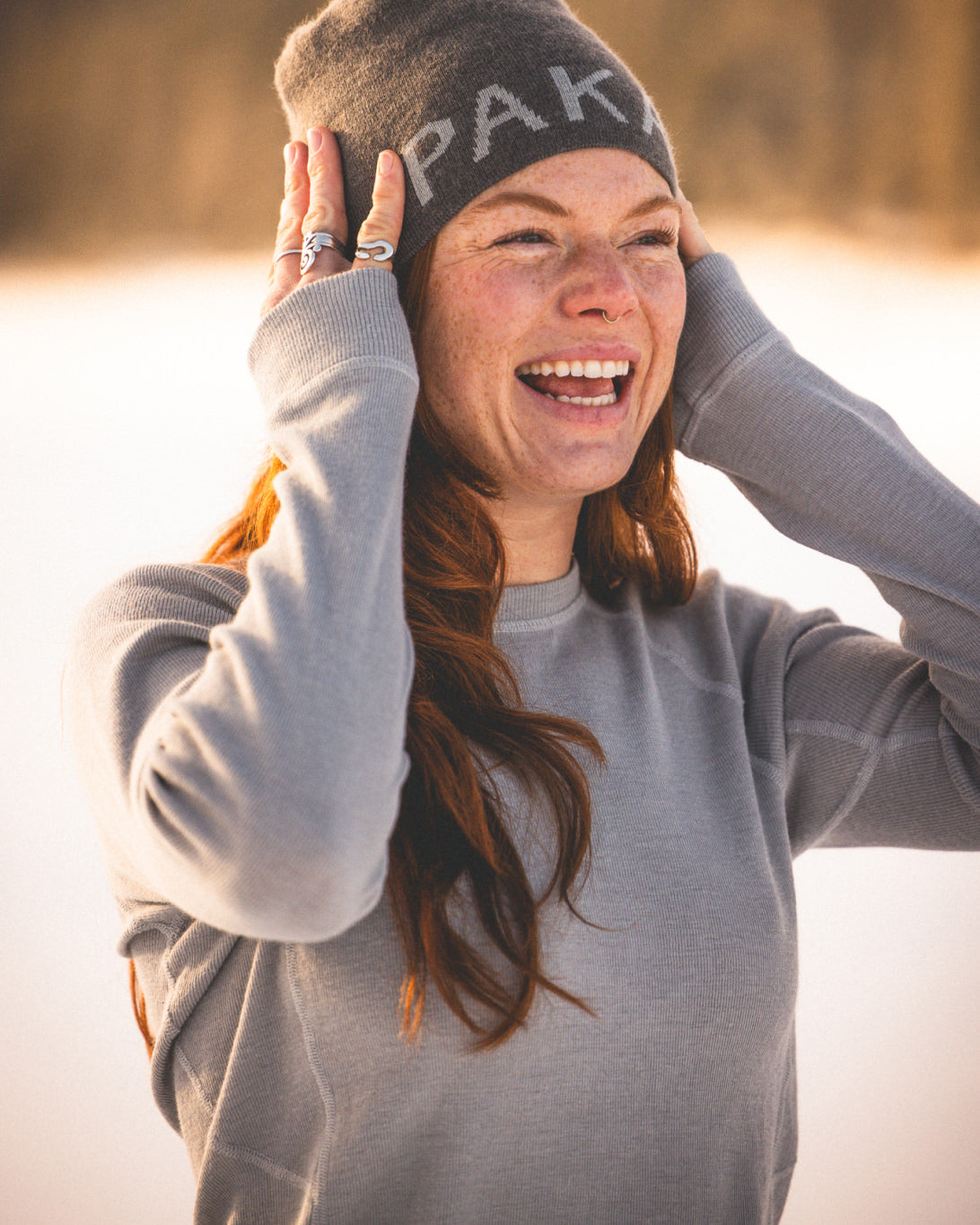 Woman Named Casey Smiling in Beanie Wearing Silver / Light Grey Alpaca Wool Thermal Baselayer Top with Snow in Background – PAKA Apparel