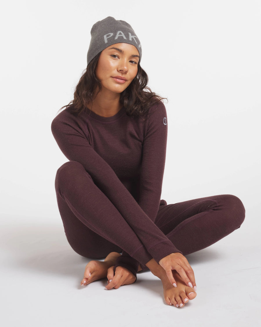 Woman in Beanie Sitting Cross-Legged in Uva / Dark Purple Alpaca Wool Thermal Baselayer Top and Bottoms – PAKA Apparel