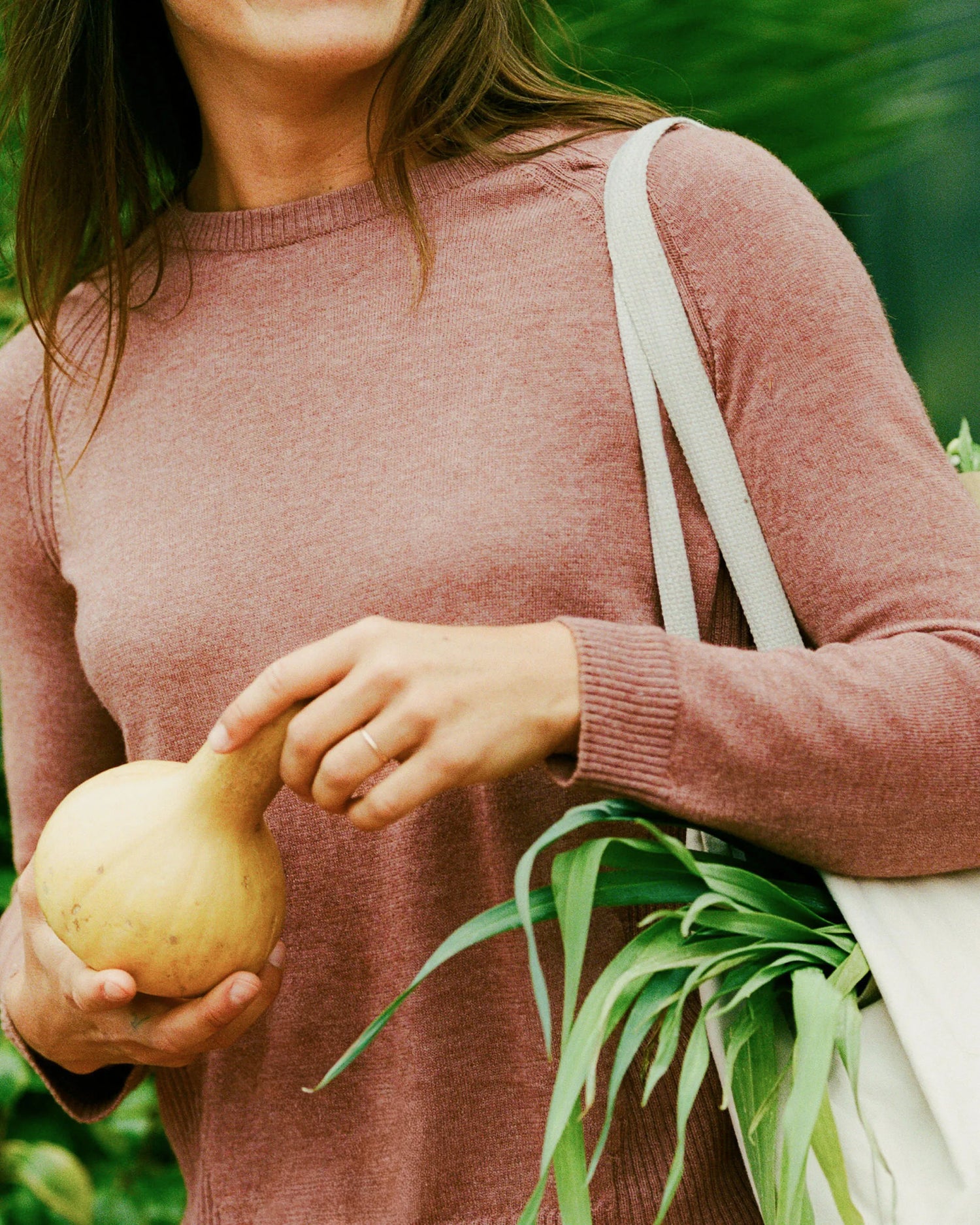 Person holding an onion and a white bag with greenery in the background