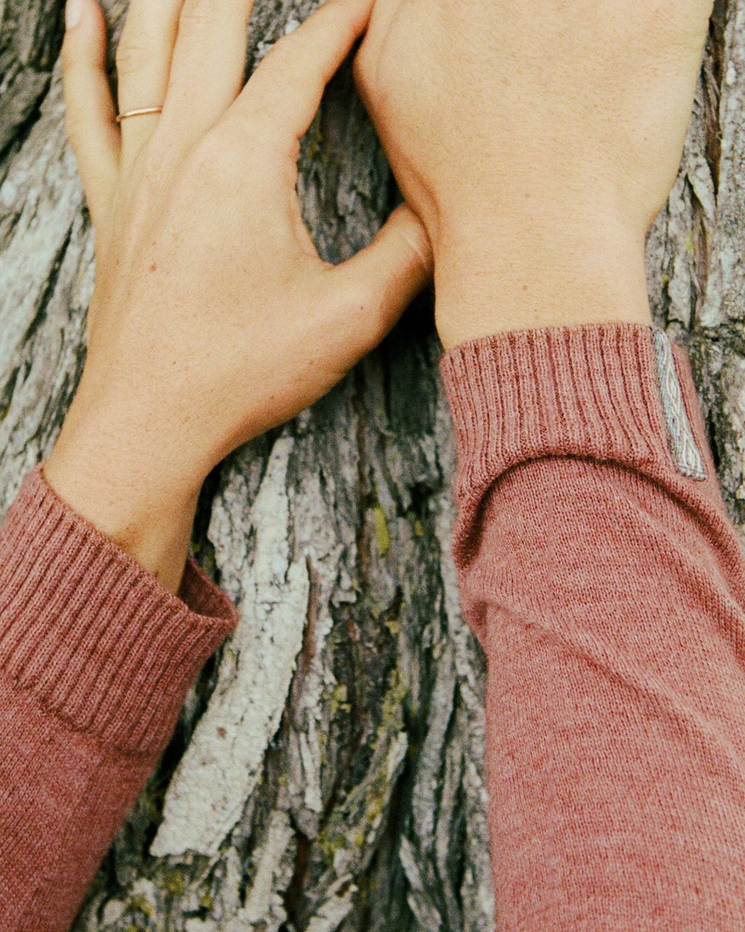 Close-up of hands wearing pink sleeves against a tree bark background
