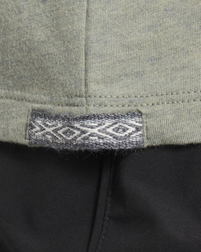Close up of Women’s Essential Tee hem showing woven Inca ID tag with diamond motif on willow fabric over black pants
