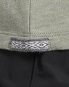 Close up of Women’s Essential Tee hem showing woven Inca ID tag with diamond motif on willow fabric over black pants