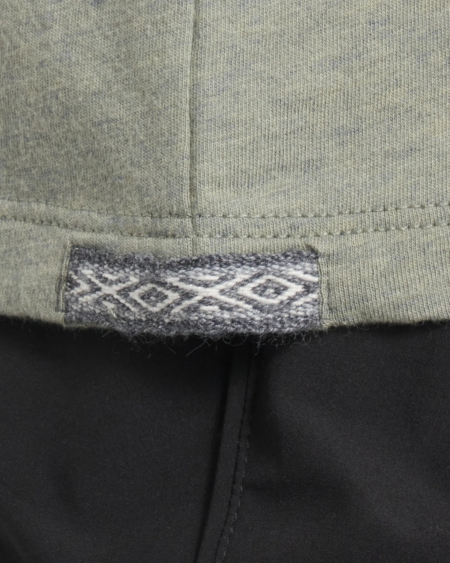 Close up of Women’s Essential Tee hem showing woven Inca ID tag with diamond motif on willow fabric over black pants