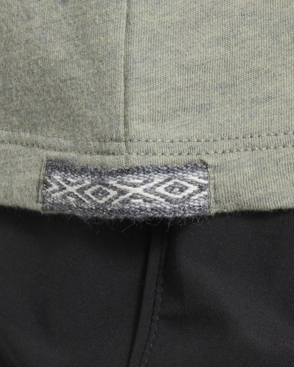 Close up of Women’s Essential Tee hem showing woven Inca ID tag with diamond motif on willow fabric over black pants