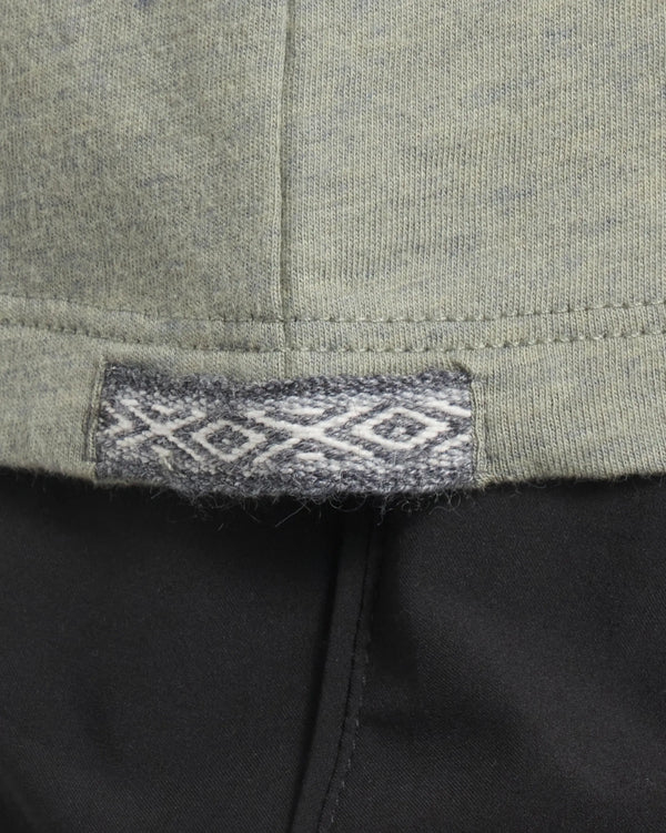 Close up of Women’s Essential Tee hem showing woven Inca ID tag with diamond motif on willow fabric over black pants