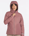 Front view of women’s Apu puffer jacket in rose, model zipping to show hood and alpaca insulation on white background