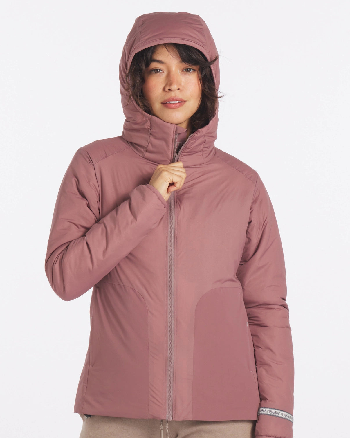 Front view of women’s Apu puffer jacket in rose, model zipping to show hood and alpaca insulation on white background