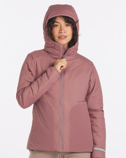 Front view of women’s Apu puffer jacket in rose, model zipping to show hood and alpaca insulation on white background