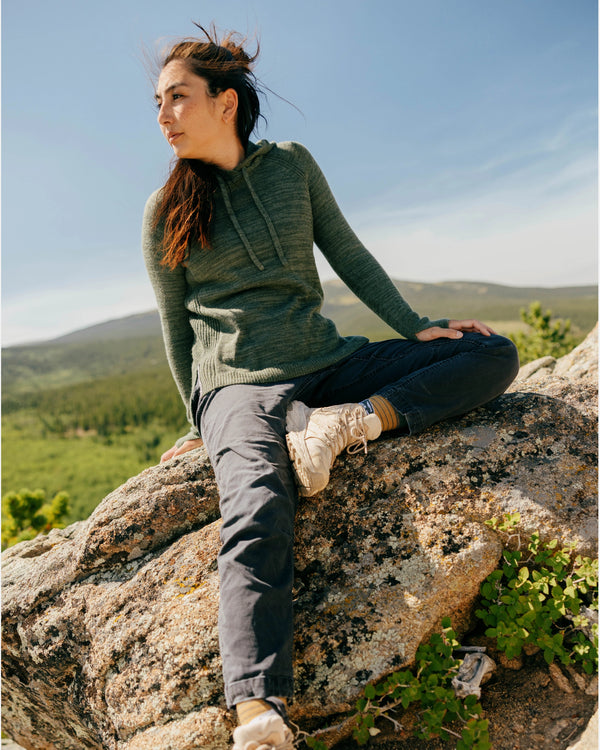 Woman sitting on a rock wearing a lightweight eucalyptus alpaca hoodie and hiking pants at a sunny mountain overlook